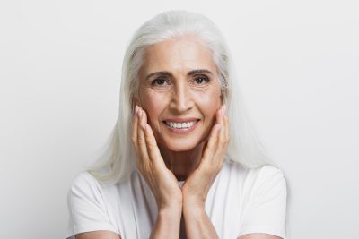 Smiling senior woman with long white hair gently holding her face, symbolizing confidence and improved appearance after spider vein treatment at PUR Skin Clinic.