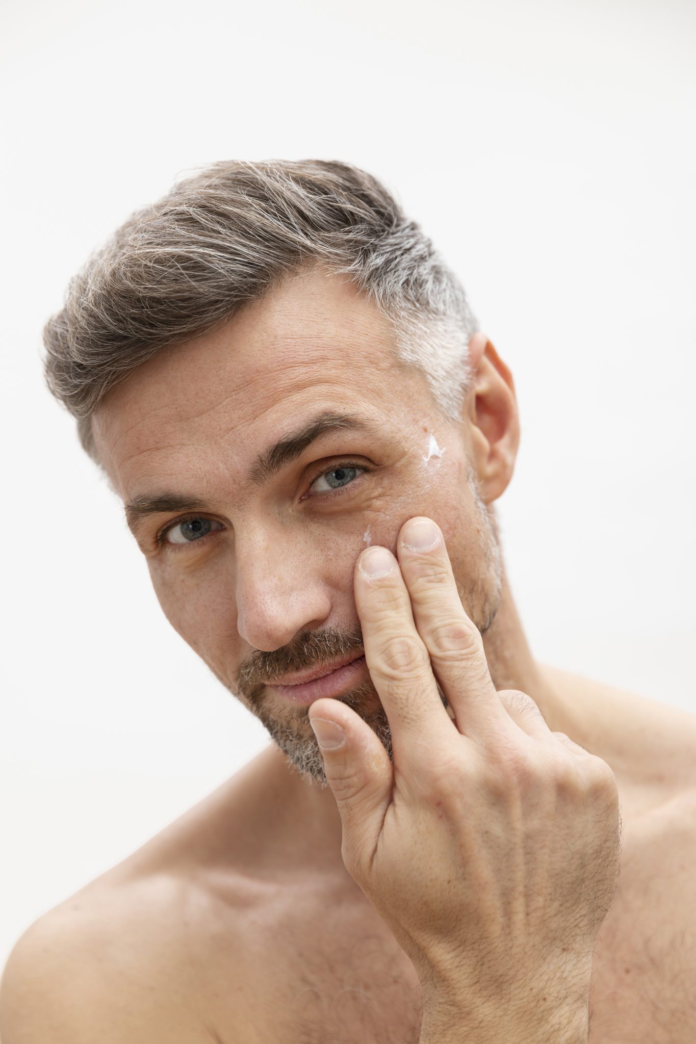 Close-up of middle-aged man applying anti-aging cream under his eyes as part of professional skincare for men at PUR Skin Clinic