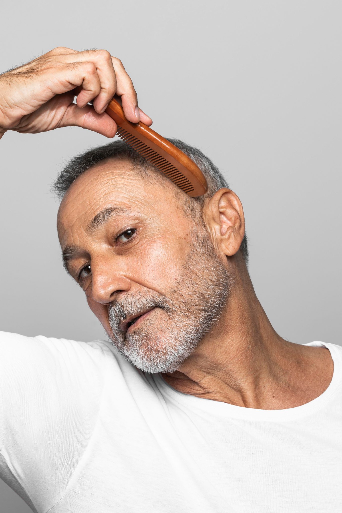 Older man combing his new growth and fuller hair after successful hair restoration treatment at PUR Skin Clinic