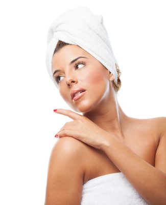 oung woman in towel wrap touching her smooth, hair-free shoulder after laser hair removal at PUR Skin Clinic