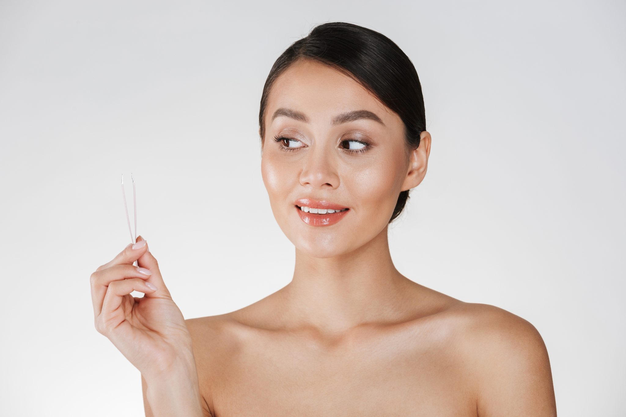Smiling woman holding tweezers and showing smooth, refined skin after laser resurfacing treatment at PUR Skin Clinic