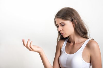 Young woman in white tank top examining her hand before treatment at PUR Skin Clinic