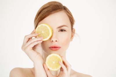 Young woman with calm, clear skin holding lemon slices to face after rosacea treatment at PUR Skin Clinic