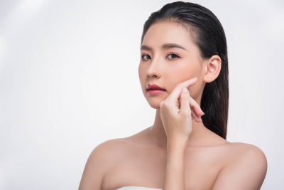 Young woman with radiant, even-toned skin gently touching her cheek, illustrating the brightening and rejuvenating effects of Moxi laser treatment.